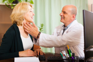 Mature doctor checking thyroid of smiling woman