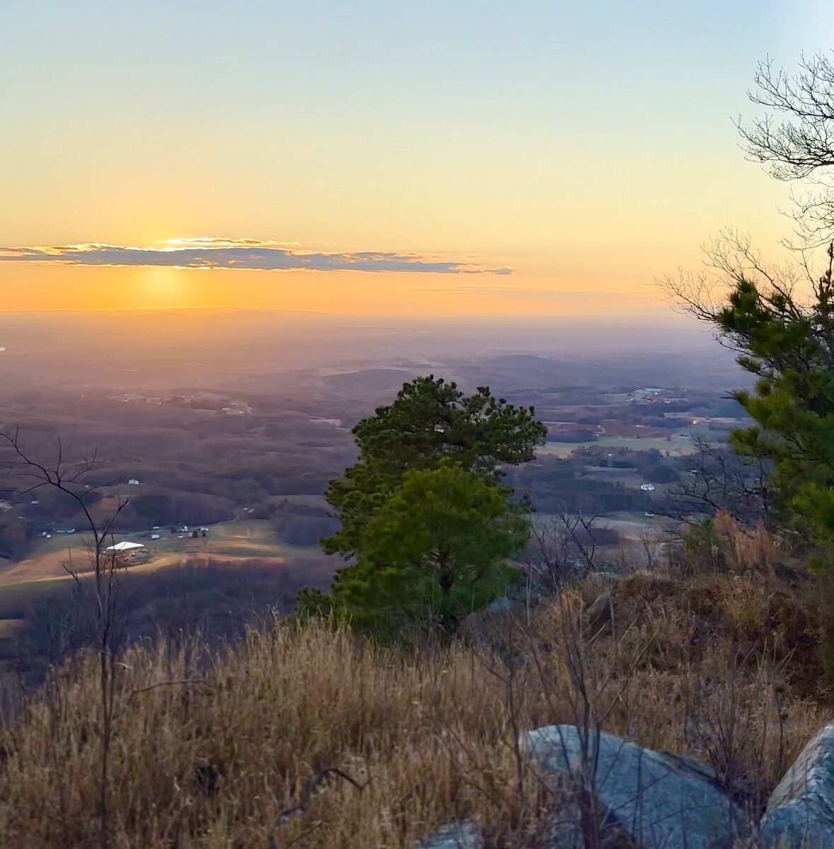 A captivating sunset at the overlook on Pilot Mountain, where the sky blazes with brilliant shades of orange and pink, illuminating the majestic landscape and the distinctive peak of the mountain.