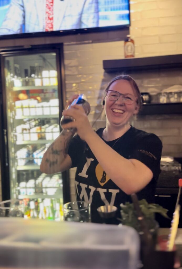 Heather, a bartender at Pies & Pints in Fayetteville, WV, skillfully crafting a cocktail, her focus evident as she pours and mixes ingredients with precision