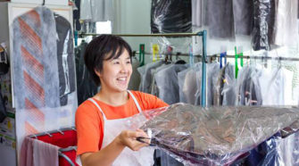 Dry cleaner handing clothing to a customer with a smile.