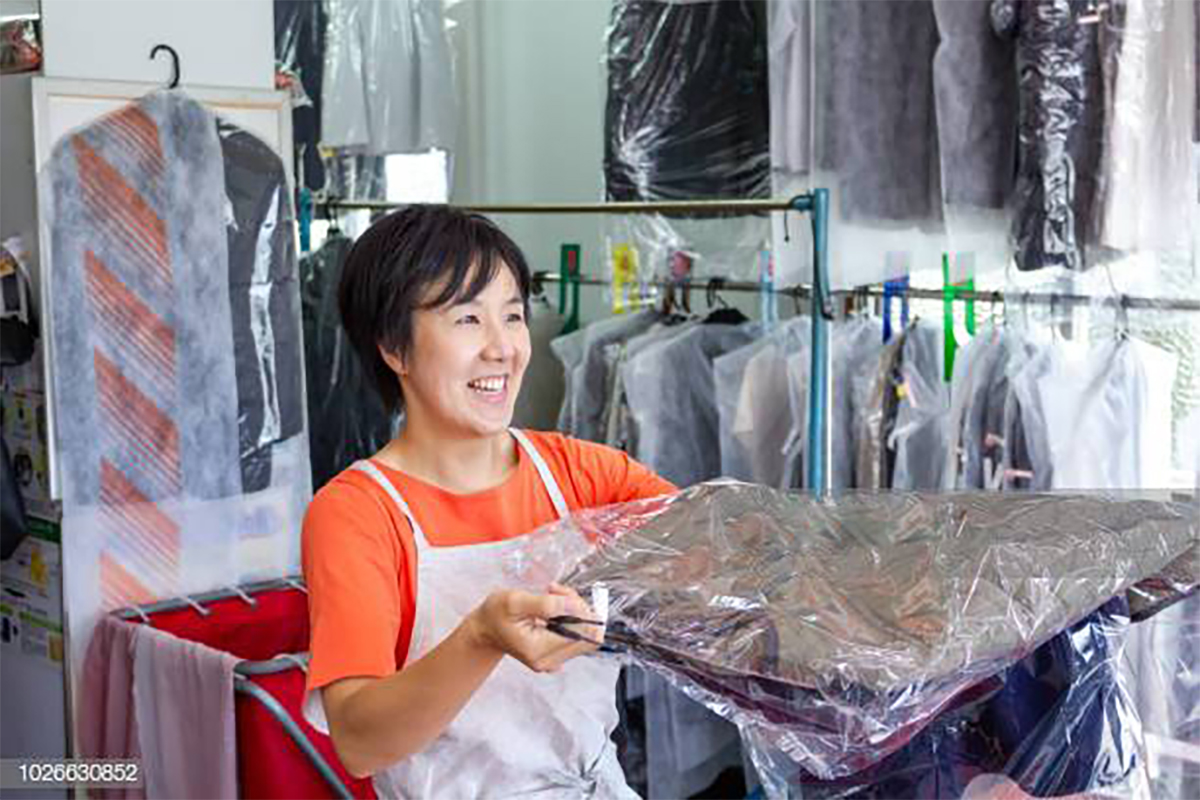 Dry cleaner handing clothing to a customer with a smile.