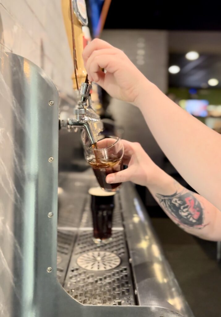 At Pies & Pints in Fayetteville, WV, a frothy glass of Bridge Brew Works root beer is served on draft, showcasing a rich, creamy head and deep amber color, symbolizing a non-alcoholic treat for patrons
