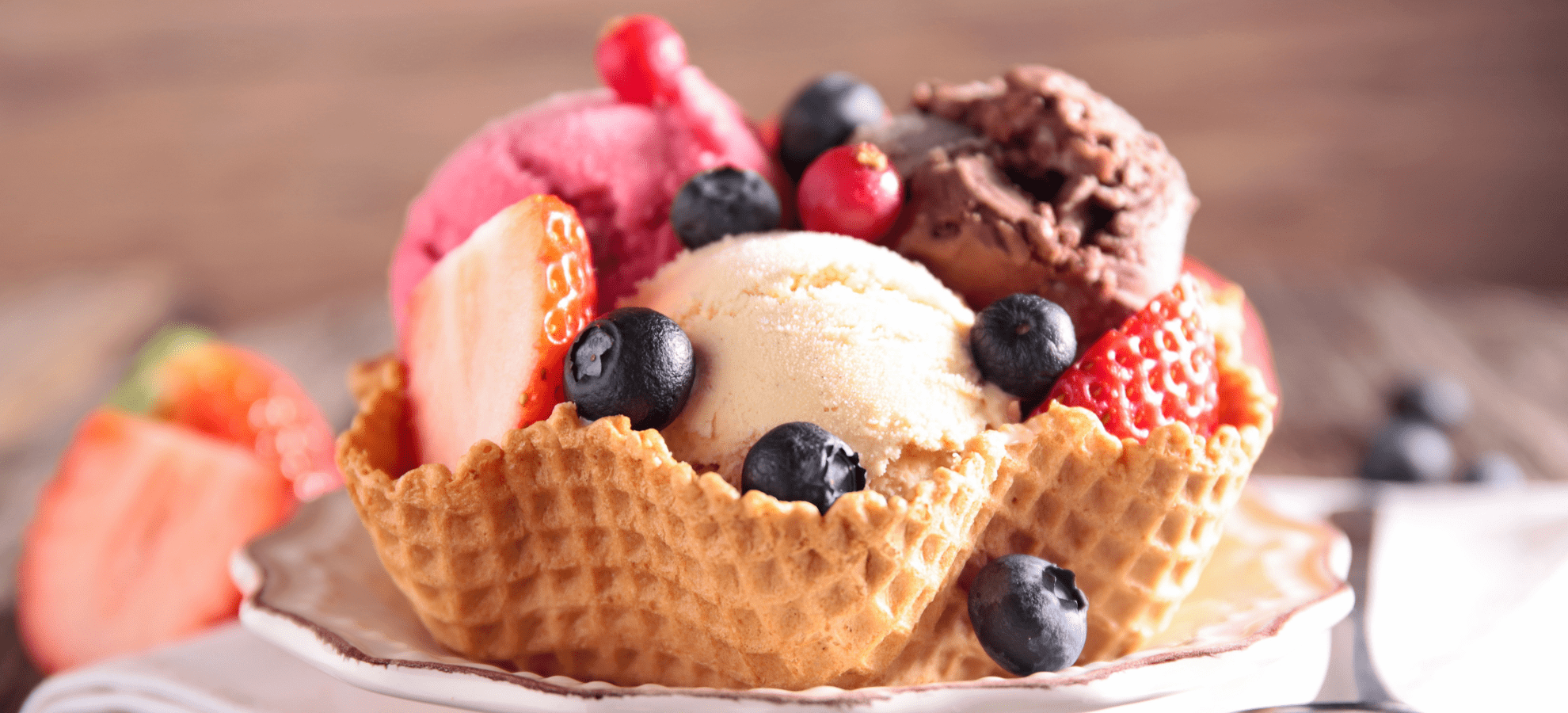 ice cream waffle bowl with straberries, blueberries and vanilla, chocolate and stratebery ice cream.