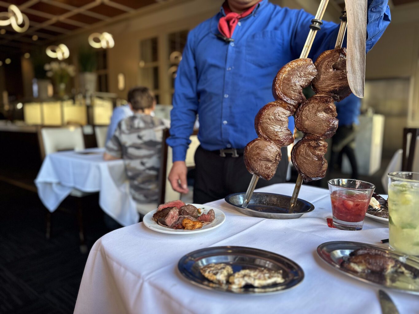 A waiter holding a large skewer of juicy, grilled meat