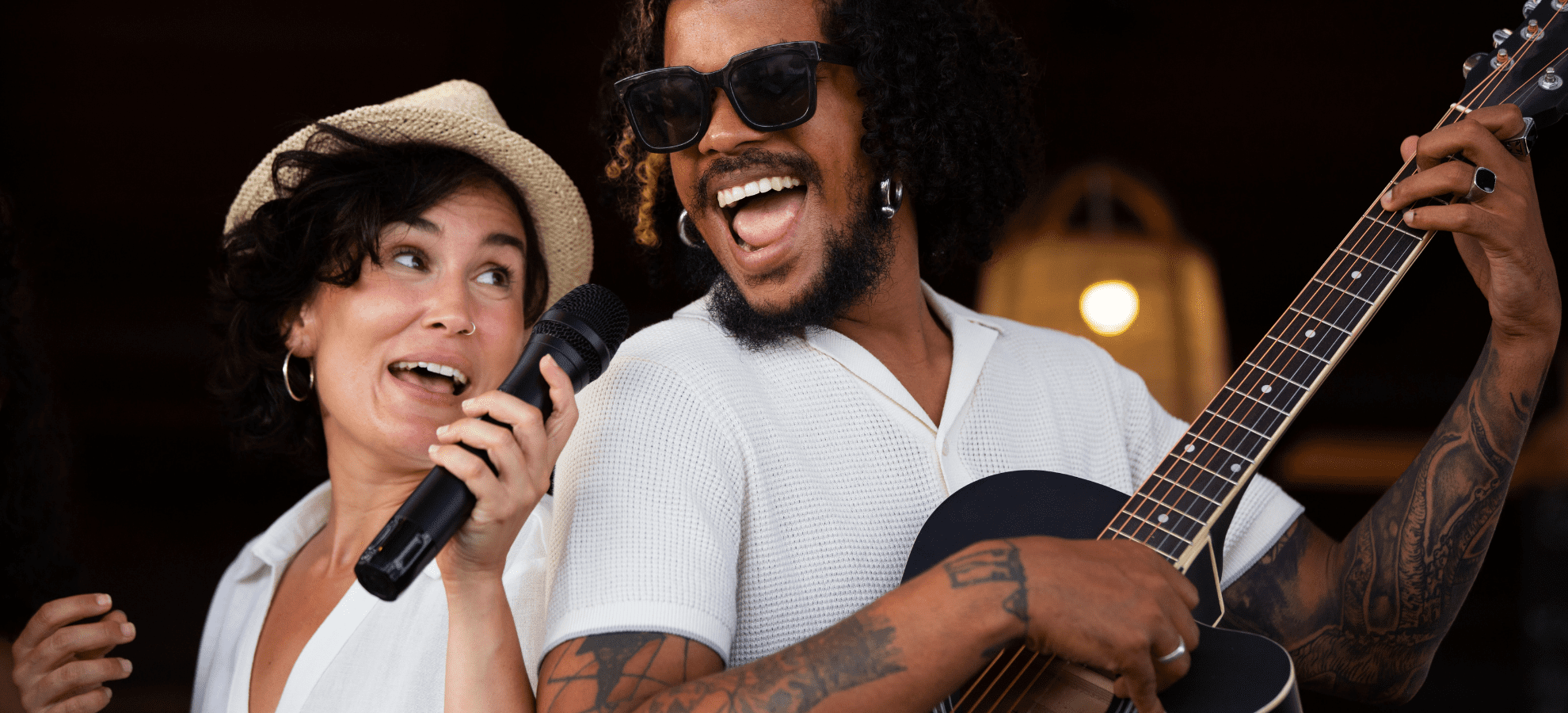 male playing the guitar and singing to a microphone and female singing leaning against the male